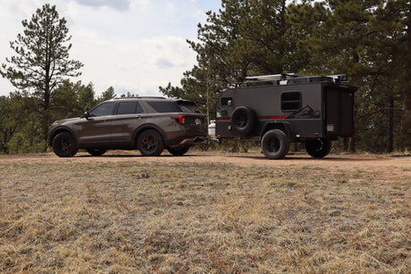 Adventure awaits! This SUV tows a rugged RV rental through a forest, ready for off-road camping.