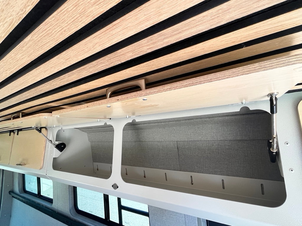 Inside a modern RV rental, showing a slatted ceiling and open overhead storage compartments with gas struts.