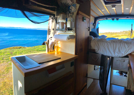 Experience van life in this rv rental! Cozy interior with kitchen, bed, and stunning ocean views protected by a mosquito net.