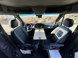 Spacious RV rental: front cabin with swiveled black seats, a wooden table, and scenic views.