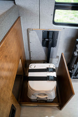 An RV rental's Dometic portable toilet, secured by straps in a pull-out wooden storage area, optimizing space.
