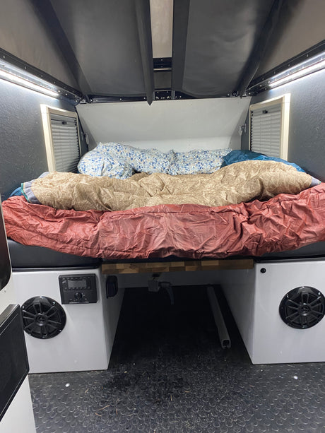 Cozy rv rental sleeping area features a bed with layered bedding, integrated lighting, side vents, and a compact audio system.