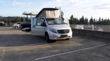 A silver Mercedes-Benz pop-top camper van, ready for adventure as an RV rental, parked on a sunlit concrete lot.