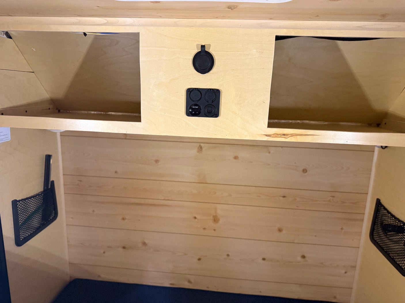 Inside an RV rental: light wood interior with overhead storage, mesh pockets, and multi-function power panel for charging.