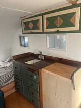 Cozy RV rental interior: custom green kitchen with copper counters, built-in sink, decorative cabinets, and bed.