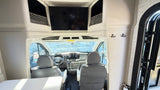 RV rental interior: View of the cockpit from the living area with TV, storage, and front seats.