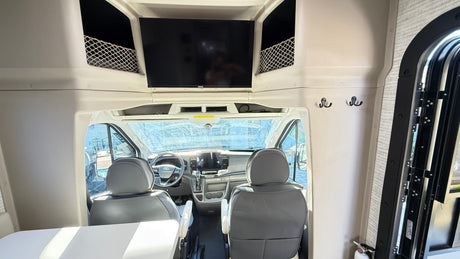 RV rental interior: View of the cockpit from the living area with TV, storage, and front seats.
