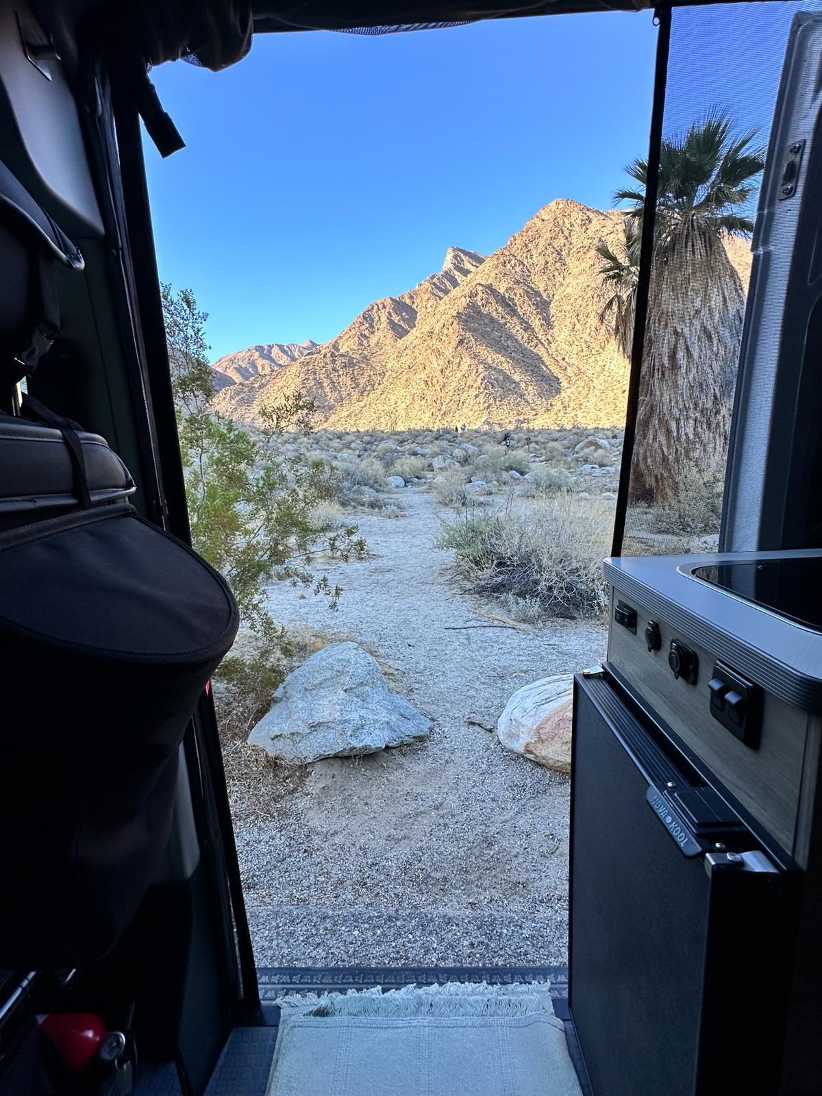  wooden cutting board on counter. Tiled backsplash with power/USB outlets.|Cozy RV rental interior with a table — photo 4