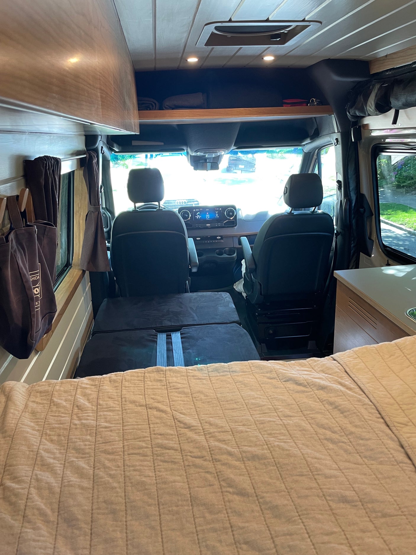 RV rental interior: A full view from the bed towards the front cockpit, featuring wood accents & overhead storage.