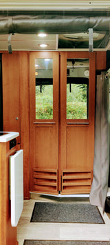 Inside an RV rental: rich wooden rear doors with windows framing lush nature. Practical interior features a kitchen area and lighting.