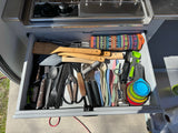 An RV rental kitchen drawer, neatly filled with diverse cooking utensils: spatulas, whisks, knives, measuring cups, and more.