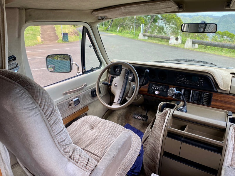 Inside an RV rental: beige interior, dashboard, steering wheel, and a view of a mountain road and green hills. — photo 9