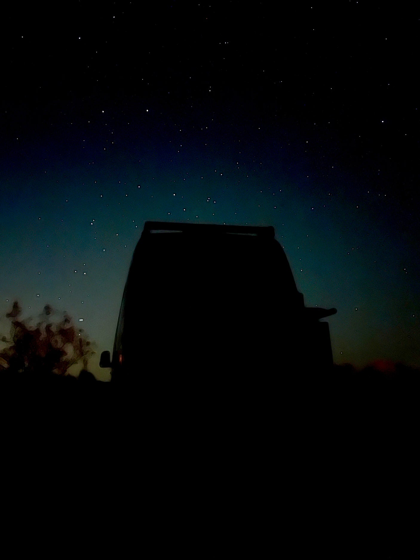 Rear view of an RV rental or van silhouetted against a vast, star-filled night sky.