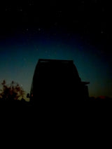Rear view of an RV rental or van silhouetted against a vast, star-filled night sky.