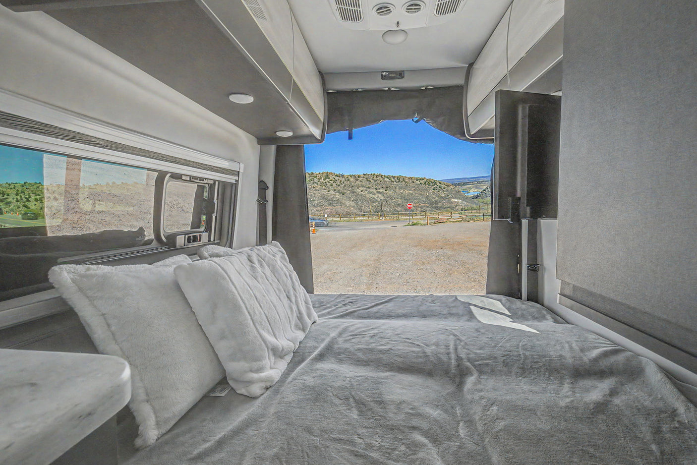 Cozy RV rental bedroom with open rear doors offering a scenic view of hills and a road, perfect for your next road trip.