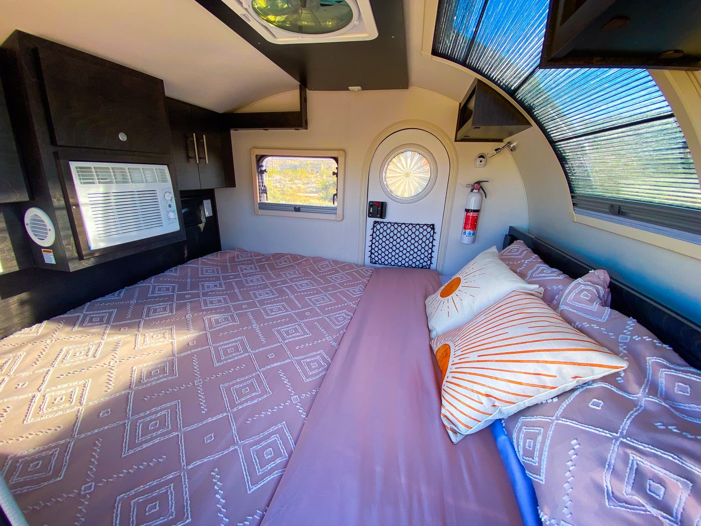 Cozy RV rental interior showing a large bed with pink bedding, an AC unit, and a unique ribbed window.