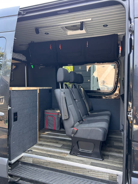 Inside an RV rental van: multi-person seating, durable flooring, smart storage, and a comfy bed area visible.