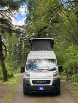 A white pop-top camper van, parked on a wooded path, ready for your next RV rental adventure in nature.