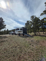 RV rental pop-up trailer & truck ready for adventure at a forest campsite with pine trees under a bright sky.