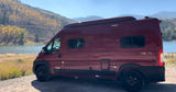 Maroon Winnebago Solis campervan by a fall lake. Explore nature with an RV rental.