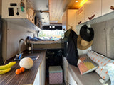 Interior of an rv rental camper van featuring a kitchen with sink, cozy bed, and living area with storage cabinets.