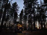 Relaxing in an RV rental camper van in a serene forest at twilight. Interior lights illuminate the cozy living space.