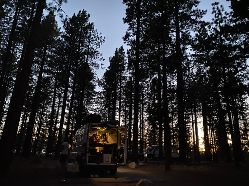 Relaxing in an RV rental camper van in a serene forest at twilight. Interior lights illuminate the cozy living space. — photo 4