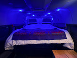 Van conversion RV rental bedroom with a comfortable bed, accented by vibrant blue LED lighting.