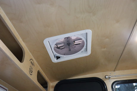 RV rental interior: Light wood ceiling with a central vent fan, overhead storage, and windows.