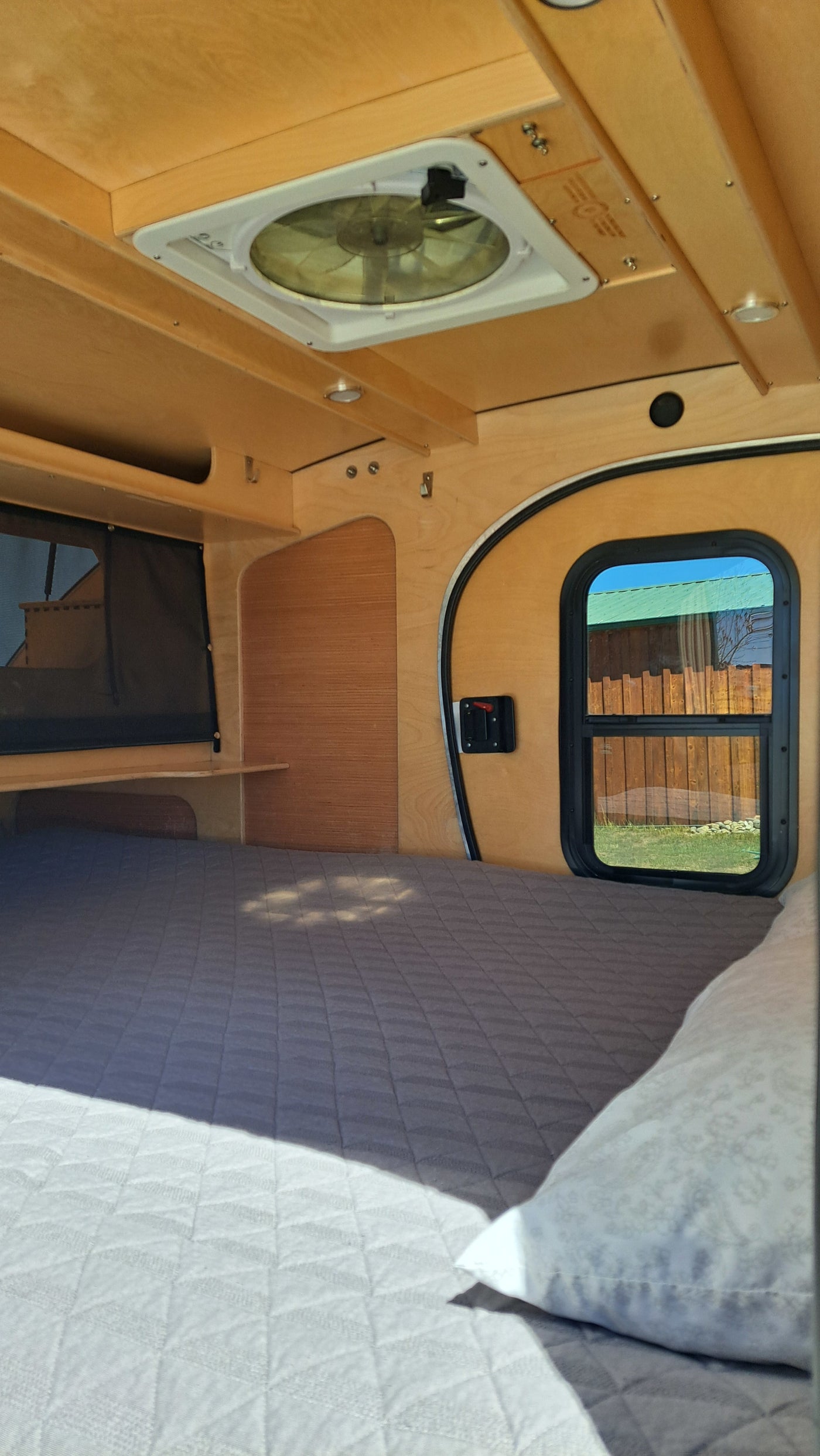 Interior of an RV rental: a warm wood-paneled sleeping area with a quilted bed, window, and ceiling fan for comfort. — photo 12