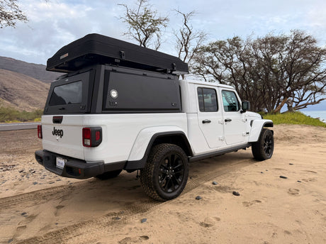 White Jeep Gladiator rv rental with a rooftop tent on a sandy coast. Ready for your next overlanding adventure.