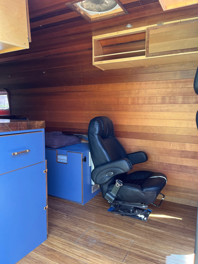 RV rental interior: rich wood walls & ceiling, black leather seating, blue custom cabinets, and a ceiling fan. Cozy comfort. — photo 11