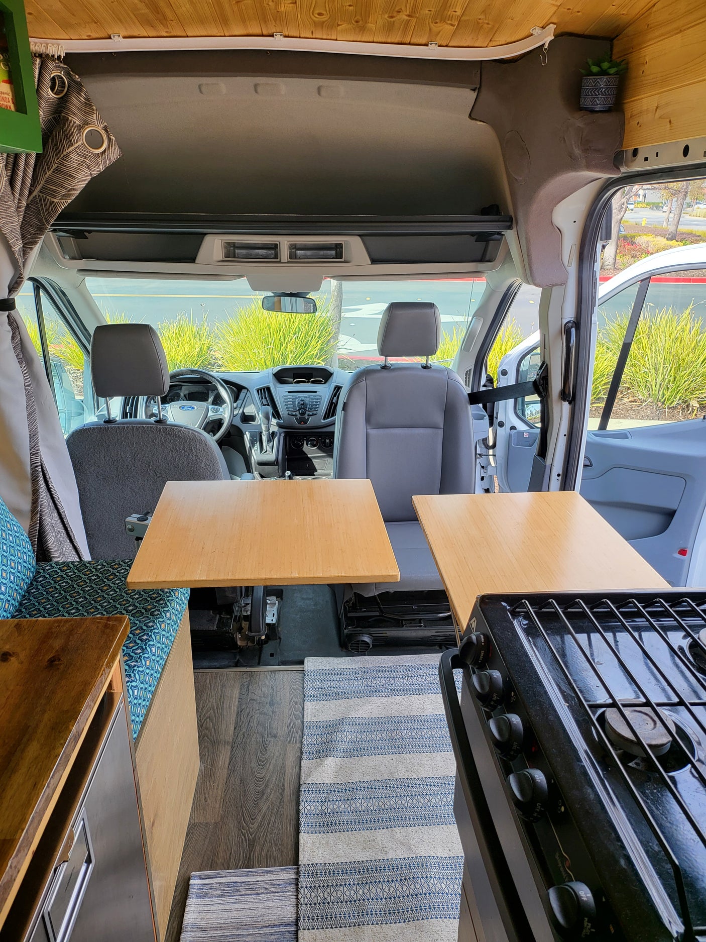 Inside this RV rental: A well-appointed camper van kitchen with stove, wooden counters, and the vehicle's front seating area.