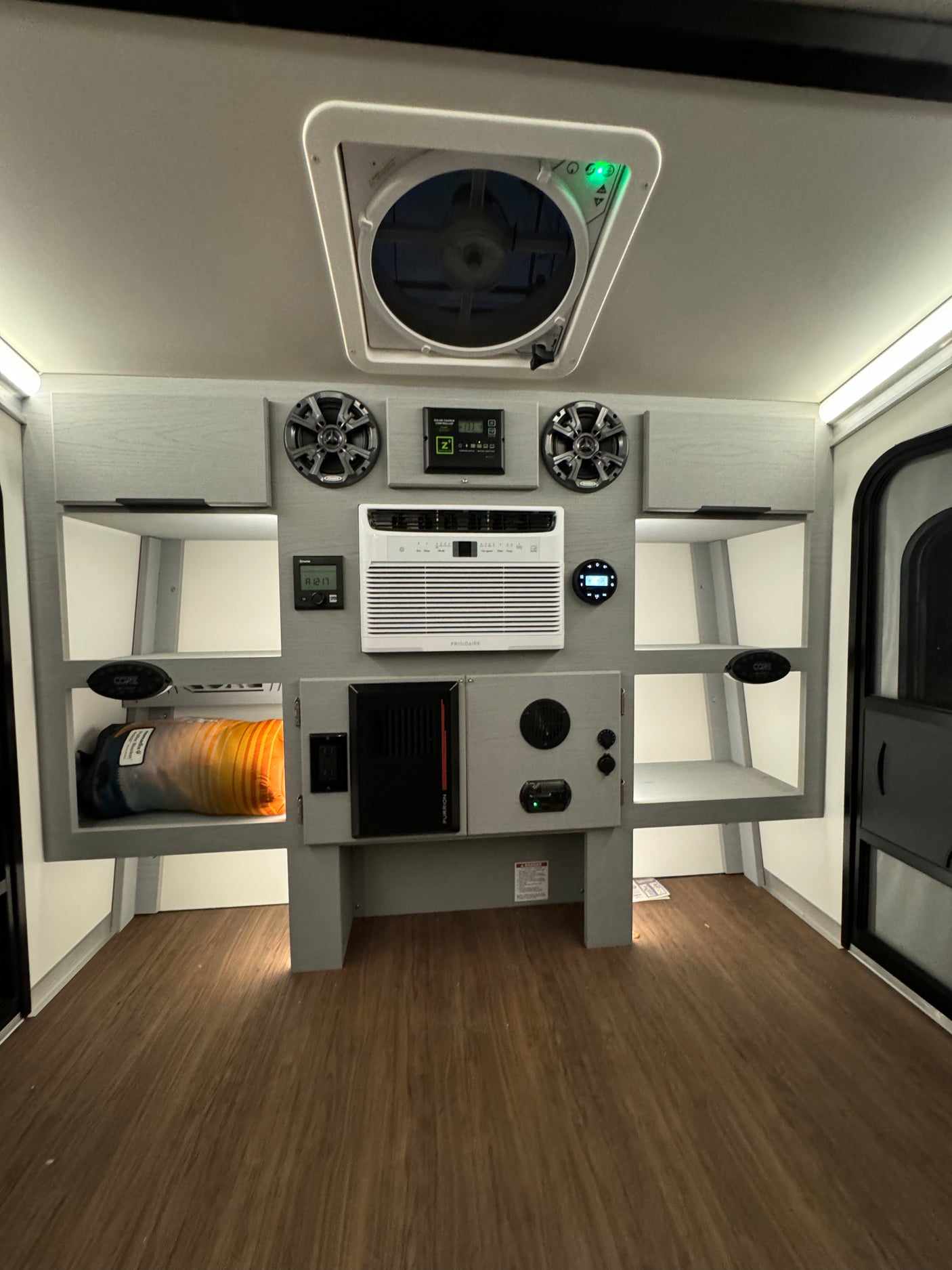 Modern RV rental interior featuring a ceiling fan, AC unit, speakers, solar control, and integrated storage for comfort and convenience.