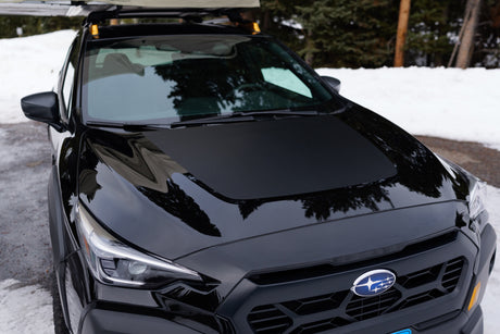 Front of black Subaru with roof rack/awning, parked in snow. An adventure vehicle for winter trips, similar to an RV rental.