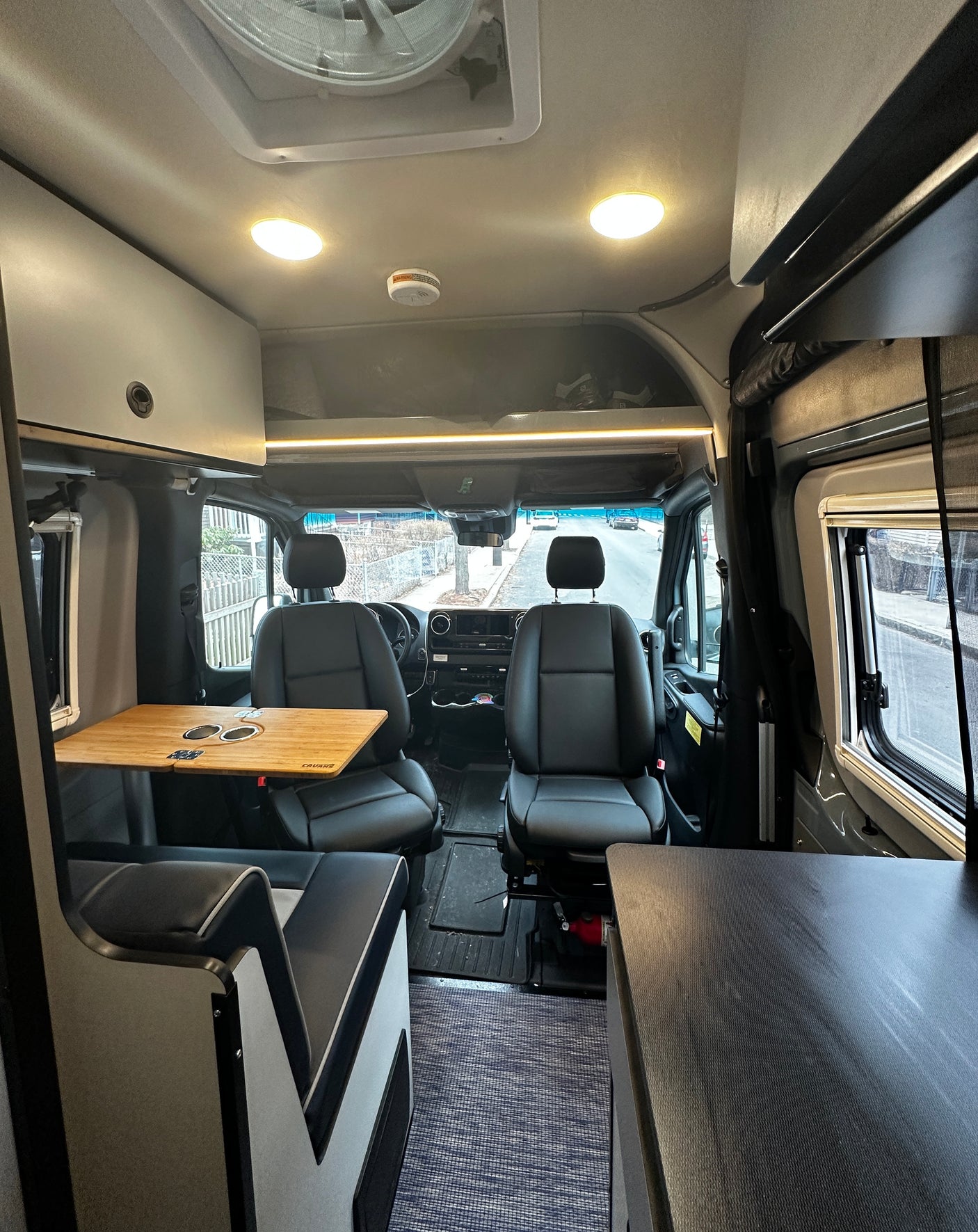 Inside this RV rental: a versatile camper van interior with front seats, side table, and overhead storage.