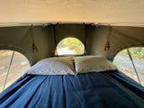 RV rental rooftop tent interior: cozy bed with blue blanket, light pillows, and nature views. Perfect for camping!