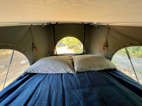 RV rental rooftop tent interior: cozy bed with blue blanket, light pillows, and nature views. Perfect for camping!