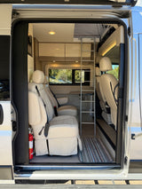 View into an rv rental showing plush cream seats, an access ladder, and a cozy interior with a scenic window view.
