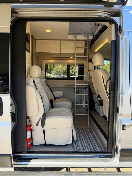 View into an rv rental showing plush cream seats, an access ladder, and a cozy interior with a scenic window view.