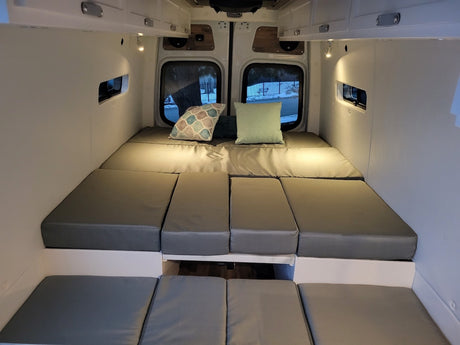 Comfortable camper van interior for your next RV rental adventure. Features modular grey bed cushions & cozy lighting.