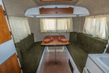 Inviting RV rental interior featuring a cozy dining nook with olive green benches & wood table set with pink dishes.
