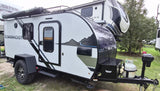 A white and black Bushwhacker rv rental, a compact off-road travel trailer with solar panels, rugged tires, and awning.