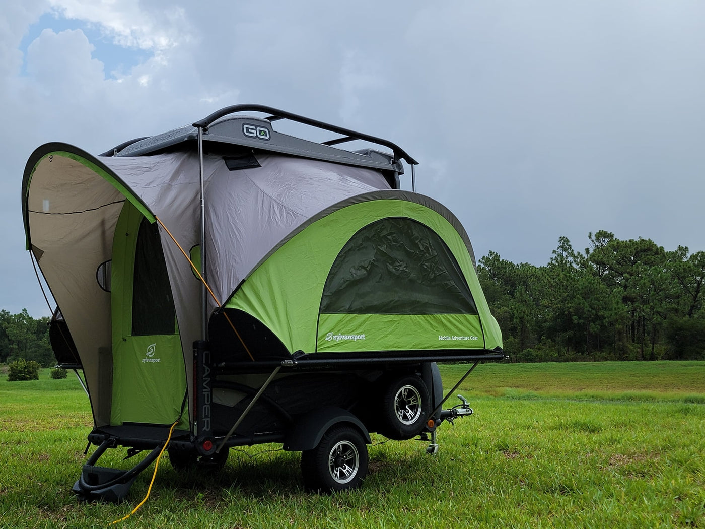 SylvanSport Go camping trailer set up in a grassy field under cloudy skies — photo 1