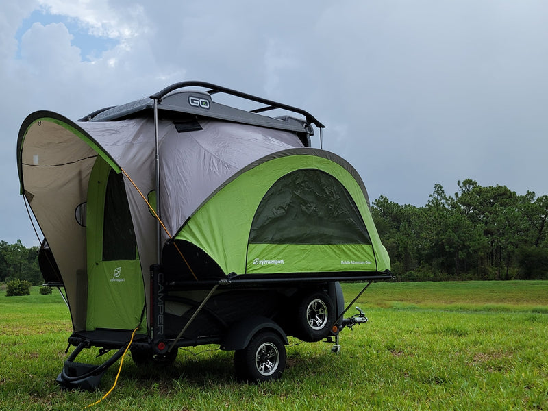 SylvanSport Go camping trailer set up in a grassy field under cloudy skies — photo 1