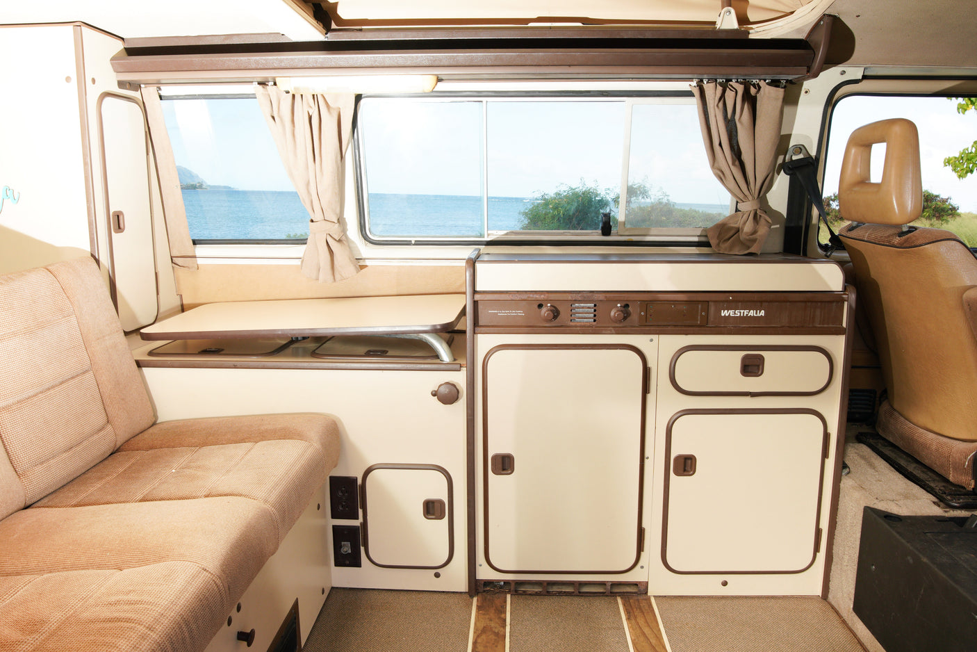 Explore a cozy Westfalia camper RV rental interior with a functional kitchenette, comfy seating, and ocean view.