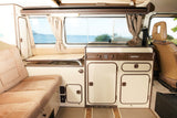 Explore a cozy Westfalia camper RV rental interior with a functional kitchenette, comfy seating, and ocean view.