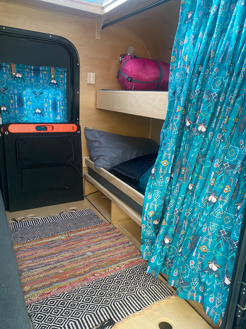 Inside a comfy RV rental: bunk beds, patterned teal curtains, and vibrant floor rugs. A cozy camper space. — photo 6