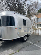 Shiny Airstream Bambi travel trailer. Consider this unique RV rental for your next trip, parked on asphalt by a fence.