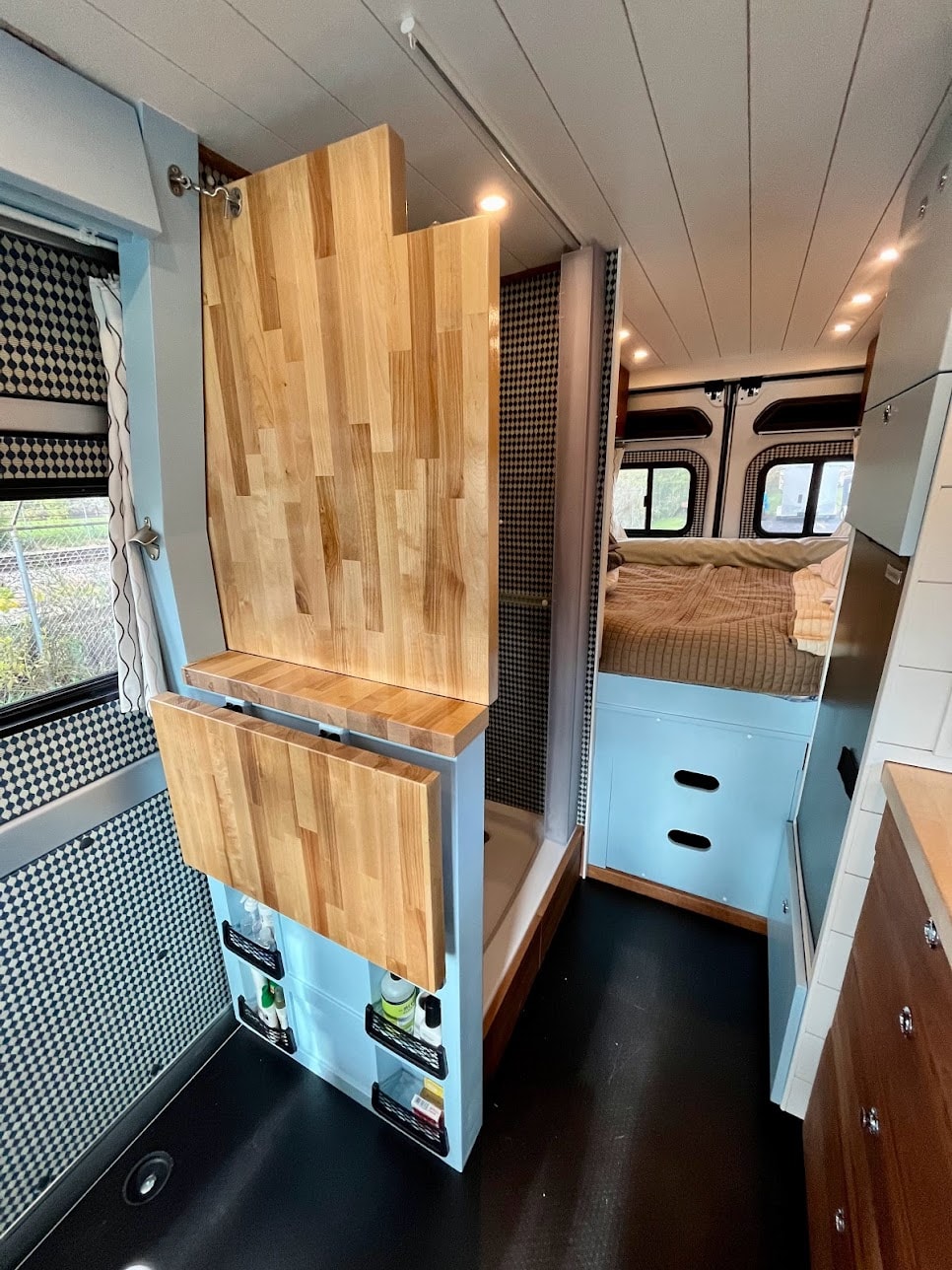 Functional camper van interior: blue cabinetry, wood accents, shower, fold-out table, bed. Great RV rental choice! — photo 11